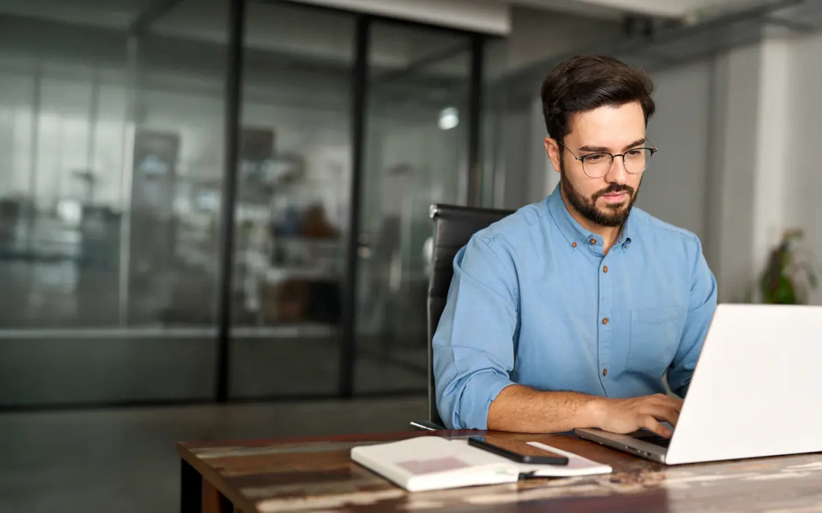 Ein Mann im blauen Hemd arbeitet am Notebook im Büro