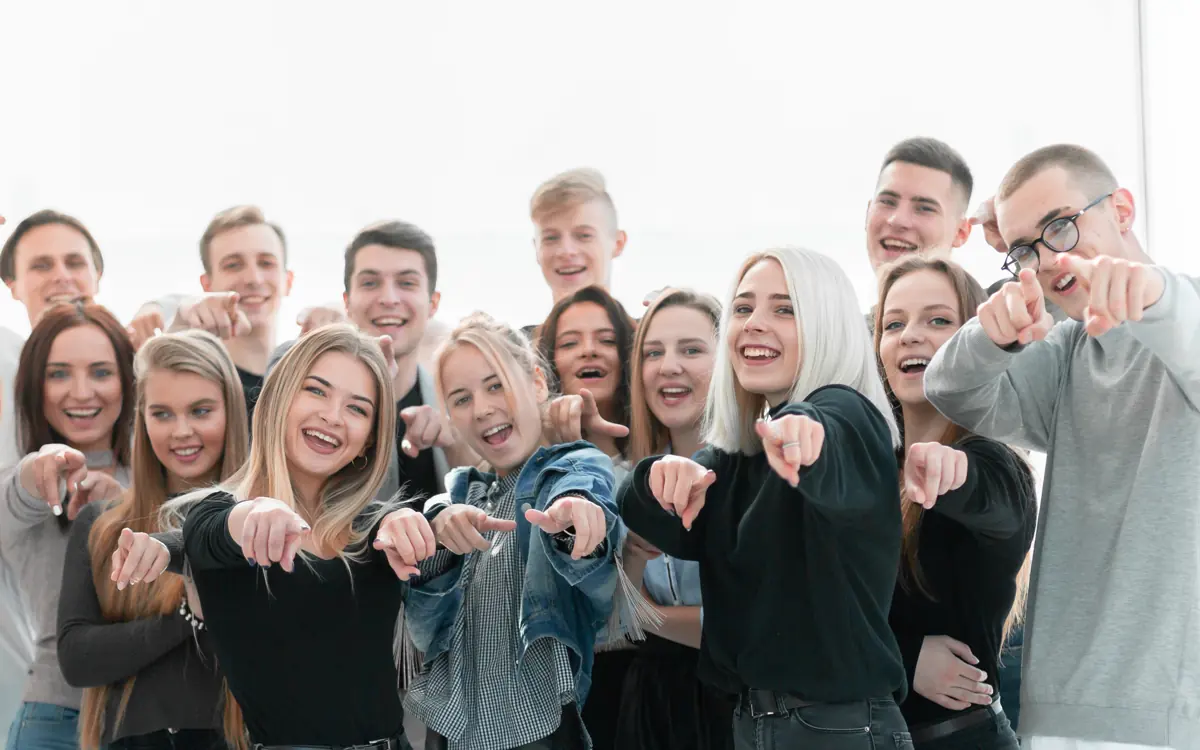 Eine Gruppe junger Leute lacht und zeigt auf die Kamera