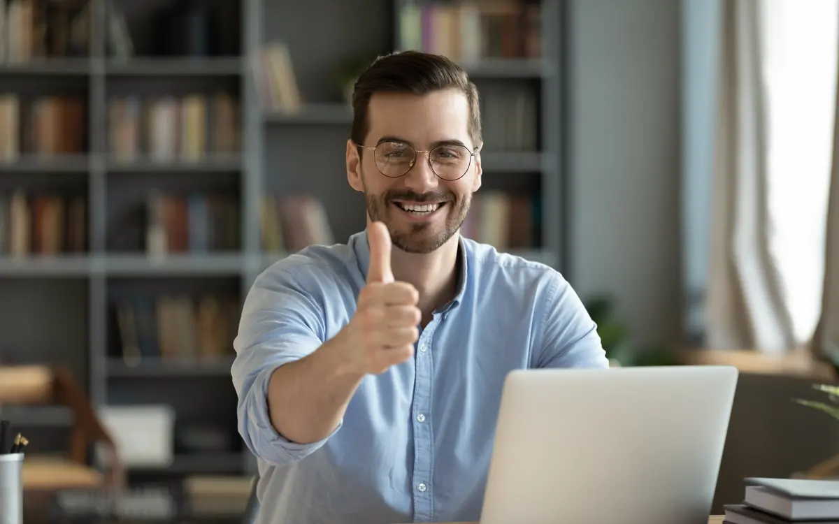 Ein Mann am Notebook hebt lachend den Daumen