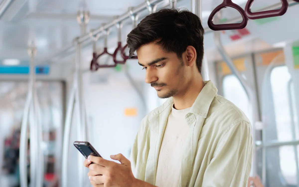 Ein junger Mann steht in der Bahn und schaut auf sein Handy