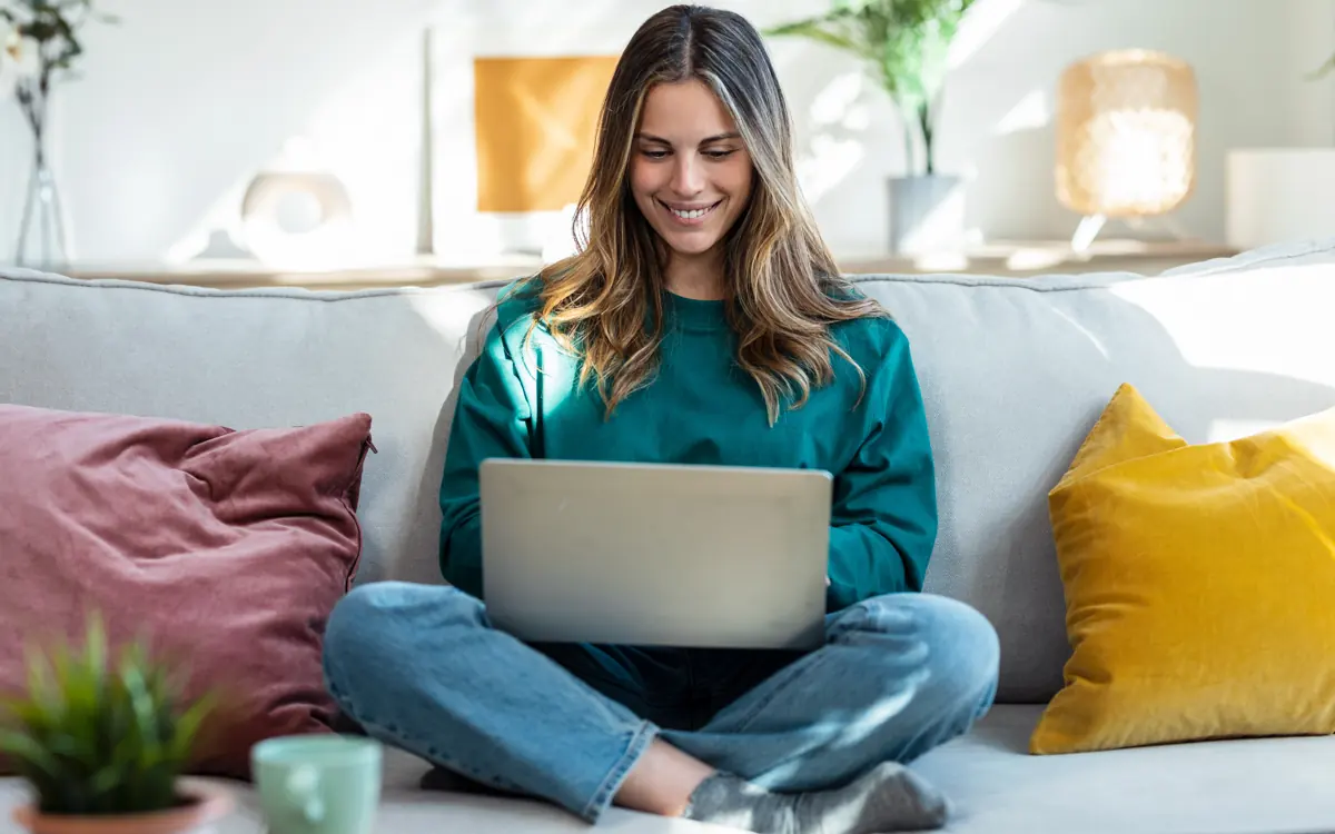 Eine Frau im grünen Pullover sitzt mit dem Notebook auf dem Sofa